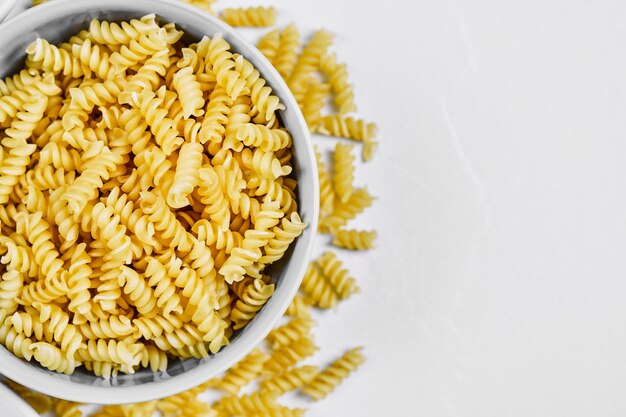 Raw fusilli and a bowl of flour on white.