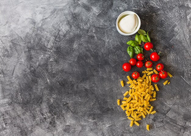 Raw fusilli with cherry tomatoes; basil leaves; black pepper and cheese on texture background