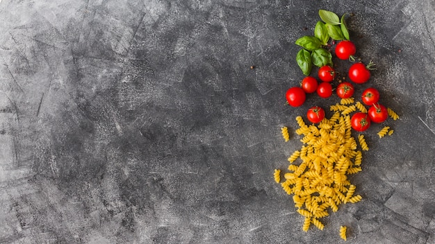 Raw fusilli with cherry tomatoes and basil leaves on texture background