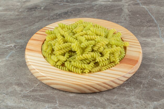 Raw green fusilli on wooden plate.