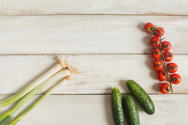 Raw green organic leeks; cucumber and cherry tomatoes on wooden desk