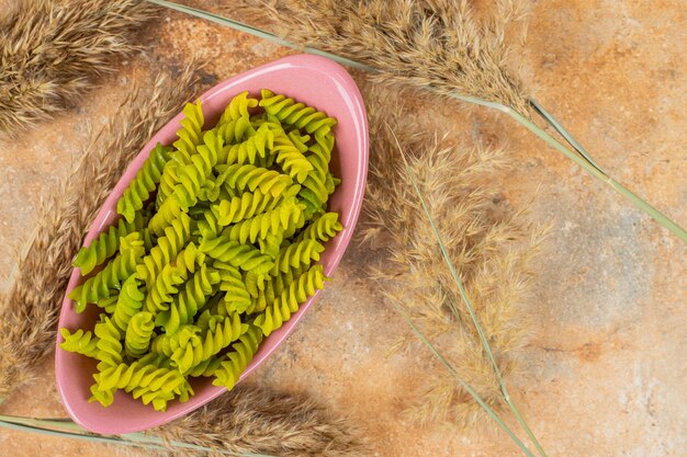 Raw green pasta fusilli in a bowl next to pampas grass , on the marble.