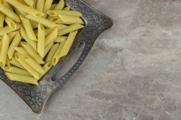 Foto gratuita pasta di penne verde cruda sul vassoio scuro.