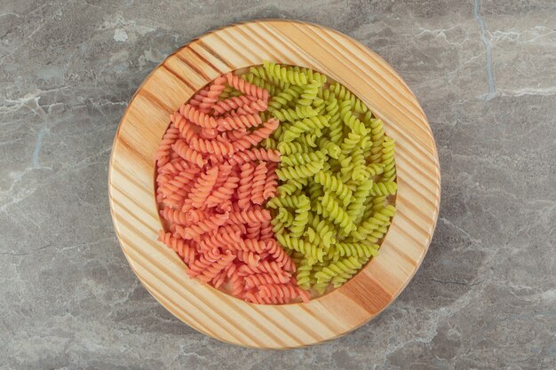 Raw green and red fusilli on wooden plate