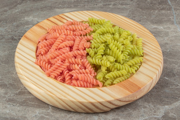 Raw green and red fusilli on wooden plate