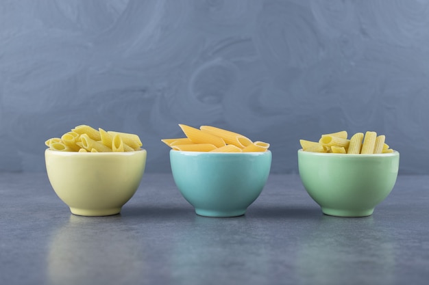 Raw green and yellow penne pasta in colorful bowls.