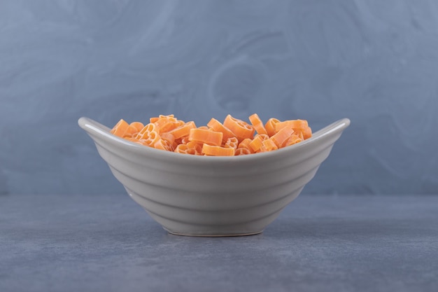 Raw heart-shaped pasta in ceramic bowl.