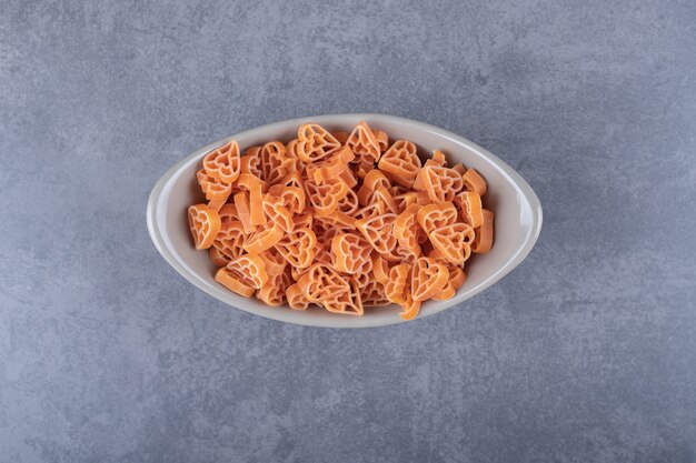 Raw heart-shaped pasta in ceramic bowl.