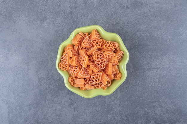 Raw heart-shaped pasta in green bowl.