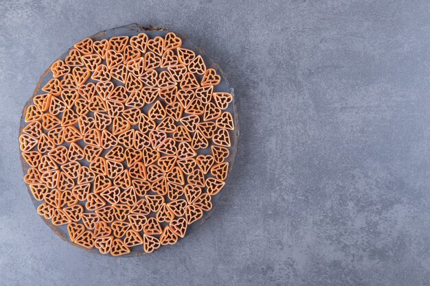 Raw heart-shaped pasta on wood piece.