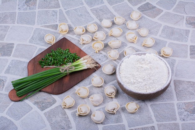 Free photo raw khinkali doughs on flour with a bunch of green onion.