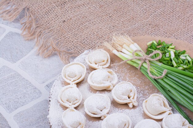 Raw khinkali doughs on flour with a bunch of green onion.