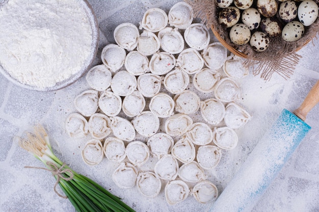 Raw khinkali doughs on the flour with a bunch of green onion.