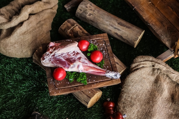 Raw lamb leg on the wooden board salt tomato greens woods top view