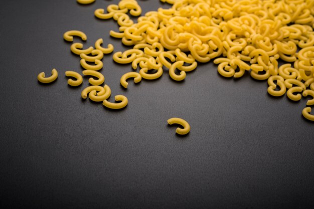 Raw macaroni pasta on black backdrop