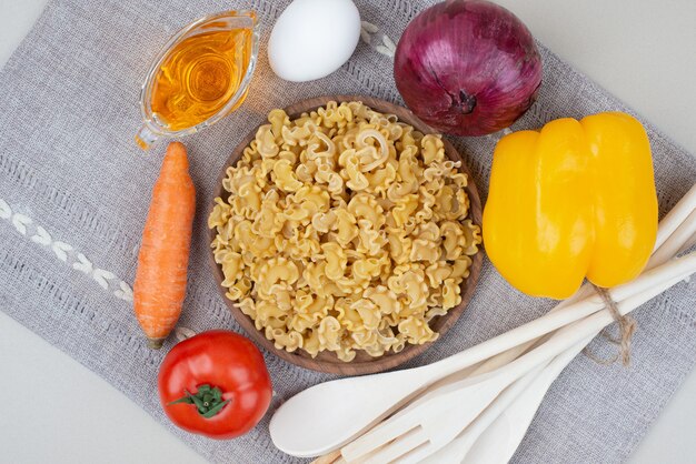 Raw macaroni with vegetables on wooden plate on tablecloth