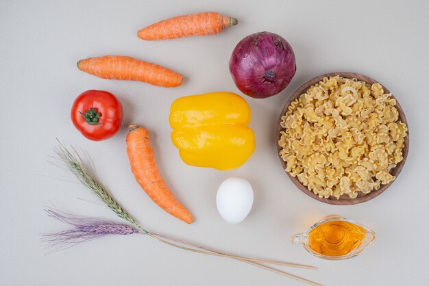 Raw macaroni with vegetables on wooden plate