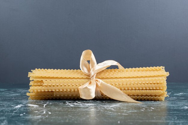 Free photo raw mafaldine pasta tied with ribbon on blue table.