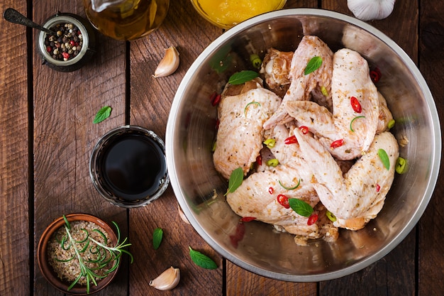 Сырые маринованные куриные крылышки, приготовленные в азиатском стиле с медом, чесноком, соевым соусом и зеленью. Вид сверху