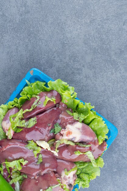 Raw meat and chicken leg on blue board.