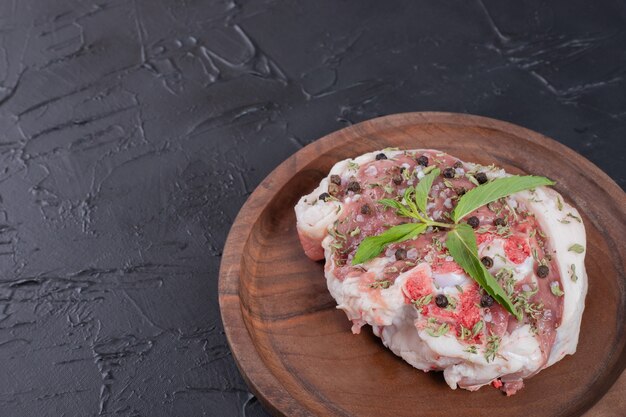 Кусок сырого мяса на деревянной тарелке, украшенный свежей мятой на темном фоне.