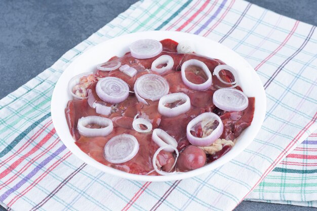 Raw meat pieces and onion slices on white plate.