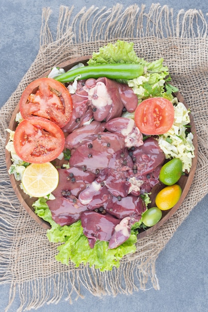 Raw meat pieces and vegetables on wooden plate.