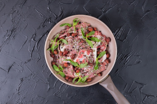 Raw meat salad with fresh mint in pan on dark surface.