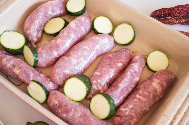 Raw meat sausages with vegetables in pan