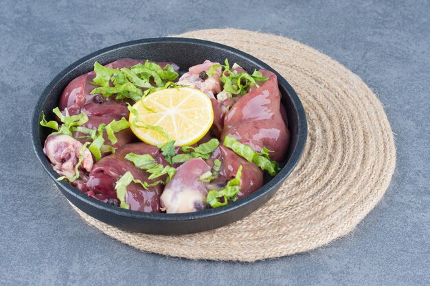 Raw meat slices and sliced lemon on black plate.