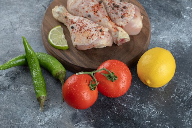 Raw organic chicken legs with ingredients for cooking on a wooden cutting board .