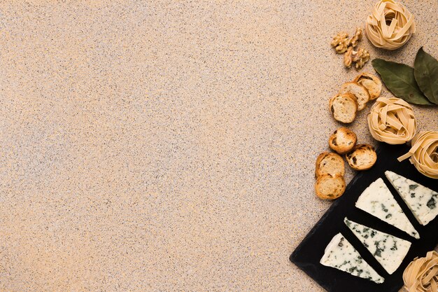 Raw pasta balls; bread slices; walnut and bay leaves with gorgonzola cheese on slate at the right side of the background