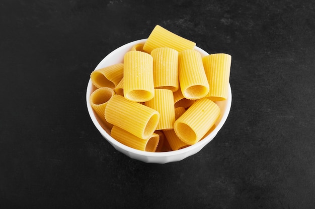 Raw pasta on black in a white cup.