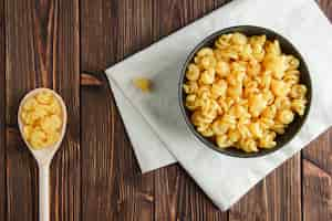 Free photo raw pasta in bowl and spoon on wooden and kitchen towel, flat lay.