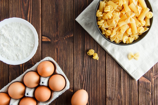 Raw pasta in a bowl with eggs, flour flat lay on wooden and kitchen towel