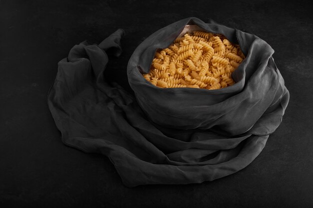 Raw pasta in a container wrapped with blue tablecloth. 