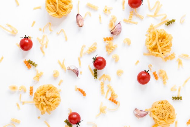 Raw pasta and fresh cherry tomato over white surface