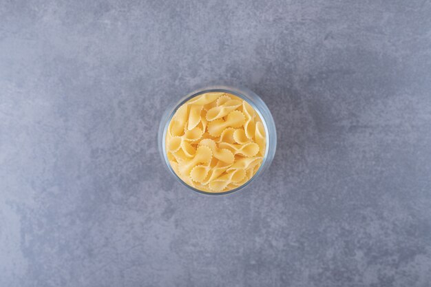 Raw pasta in glass on stone background.