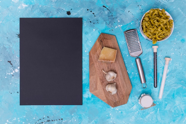 Free photo raw pasta ingredient; slate; chopping board and grater on stained backdrop