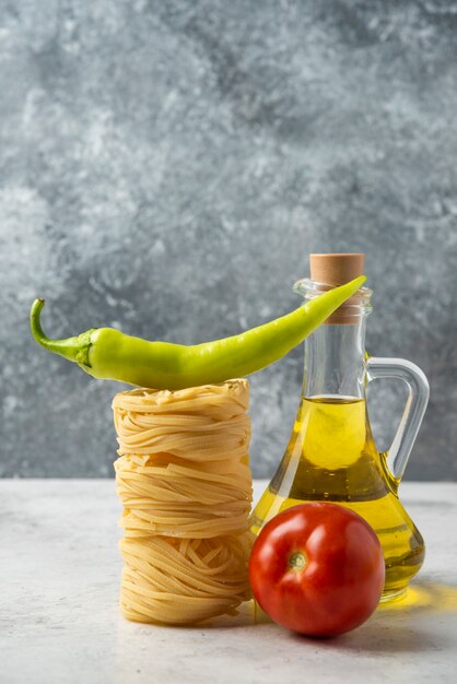 Free photo raw pasta nests, bottle of olive oil and vegetables on white table.