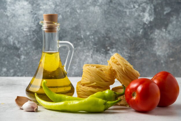 Raw pasta nests, bottle of olive oil and vegetables on white table. 