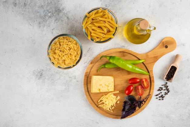 Raw pasta, oil, cheese and fresh vegetables on marble.