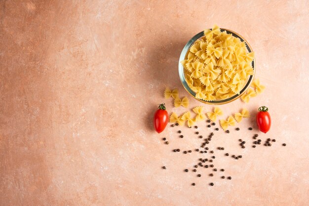 Raw pasta, pepper grains and fresh tomatoes on orange.