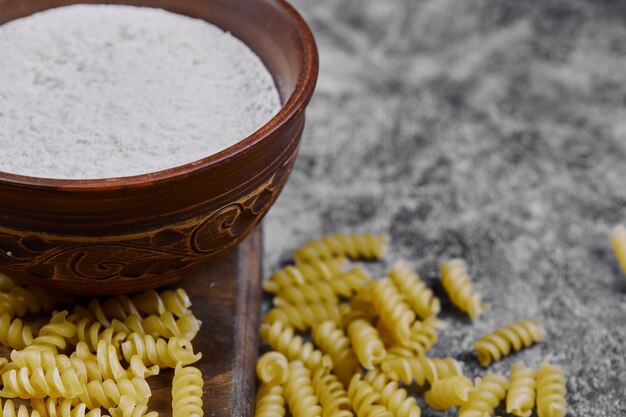 Raw pasta scattered on marble table with a bowl of flour.