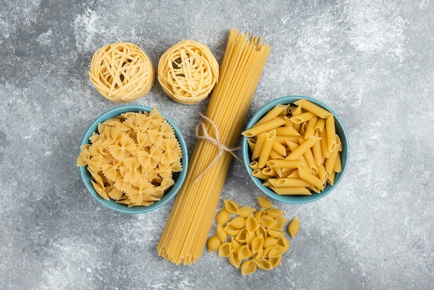 Raw pasta and spaghetti varieties on marble table.