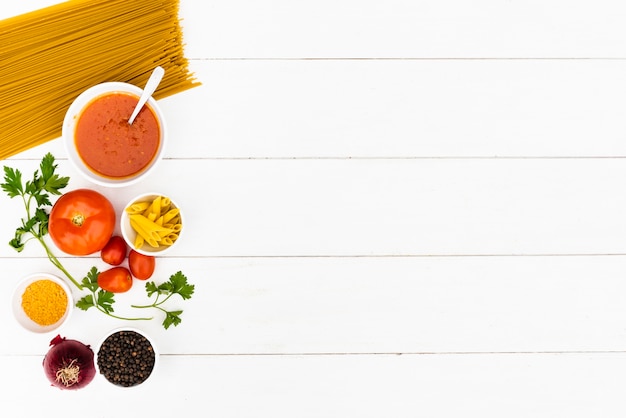 Raw pasta and tasty ingredient over white wooden table