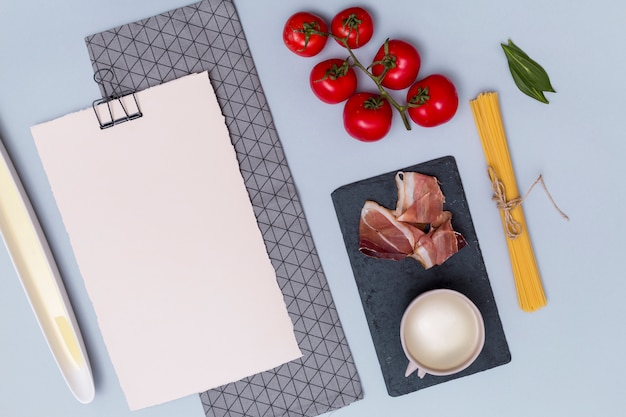 Сырые макароны; томаты; мясо; белый соус; лавровый лист и чистая белая бумага с салфеткой на простом фоне