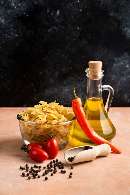 Free photo raw pasta, vegetables and bottle of oil on orange table.