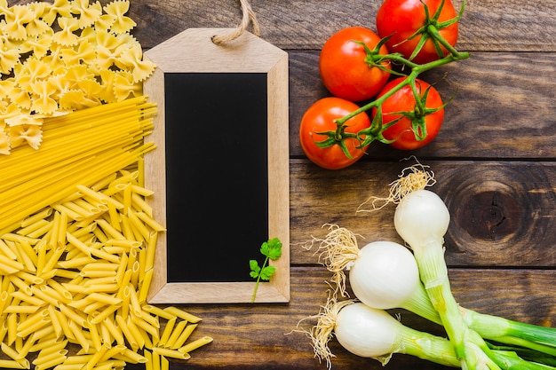 Raw pasta and vegetables near blackboard