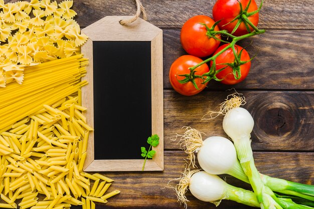 Raw pasta and vegetables near blackboard